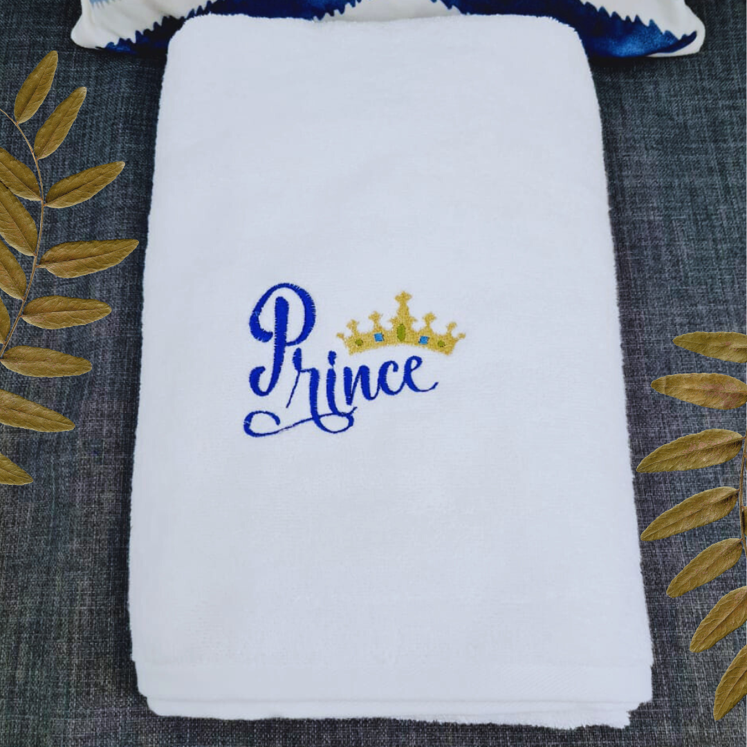 Prince embroidered bath towel folded with a golden leaf decor on a dark background.