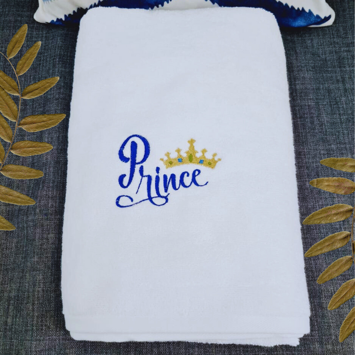 Prince embroidered bath towel folded with a golden leaf decor on a dark background.